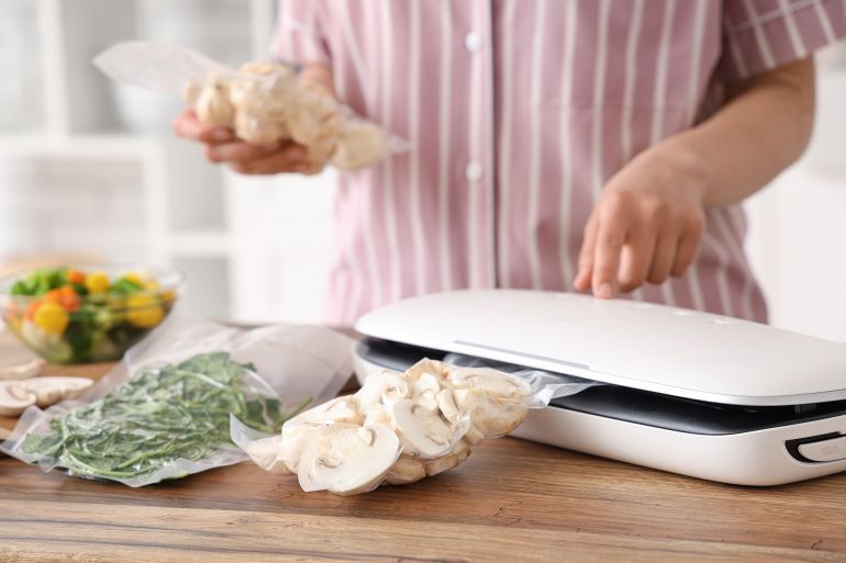 Young woman with vacuum sealer machine for food, parsley and mushrooms in packs on kitchen table المصدر: أدوبي ستوك