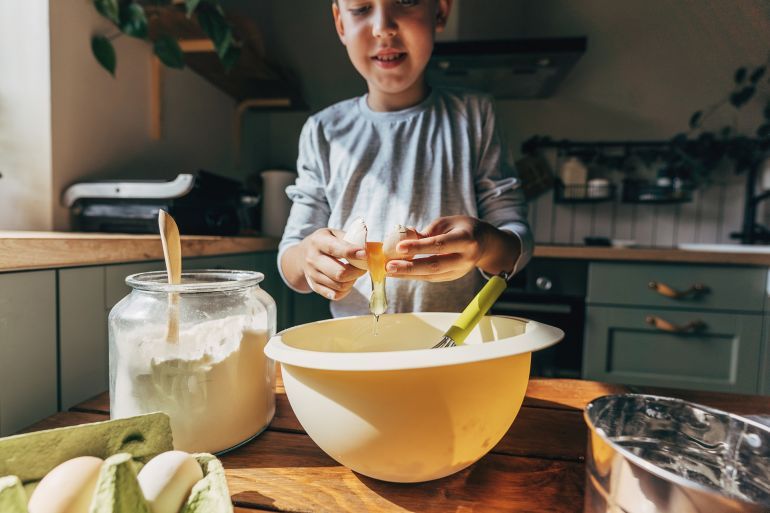 Exited boy cooking cookies at home close-up breaking egg