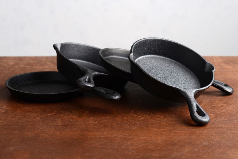 pile of cast iron skillets on old wood table; Shutterstock ID 2129927645; purchase_order: aj; job: ; client: ; other: