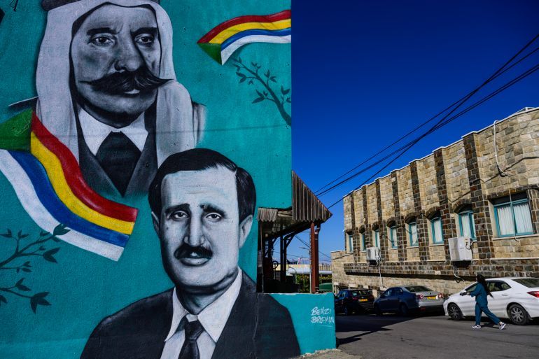 A woman walks past a mural depicting Lebanese Druze politician Walid Jumblatt (bottom, R) and Syrian Druze nationalist leader Sultan al-Atrash, in the predominantly Druze city of Beit Jann on November 16, 2023. Around 150,000 Druze, Arab adherents of an esoteric offshoot of Shiite Islam, live in Israel. Most identify as Israelis and the men -- not women -- are conscripted into the military, many serving in combat units. The Druze community is concentrated in 16 villages in northern Israel, among them Beit Jann, where Harb's funeral took place on Sunday. (Photo by John MACDOUGALL / AFP)