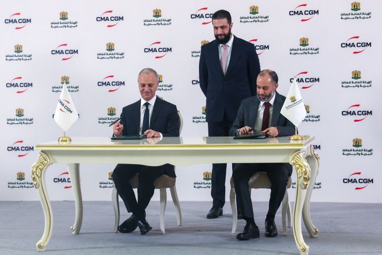 Syrian President Ahmed al-Sharaa (C) looks on as Joseph Dakak, the regional director of French shipping company CMA GGM, (L) and Latakia port director Ahmed Mustafa sign an agreement in Damascus on May 1, 2025.