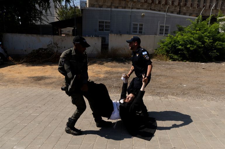 RAMAT GAN, ISRAEL - AUGUST 5: Police officers disperse an an Ultra Orthodox Jewish protester during a demonstration against drafting to the Israeli military near a recruitment base on August 5, 2024 in the Tel HaShomer area of Ramat Gan, Israel. Hundreds of Ultra-Orthodox men who were previously exempted from military service were due to arrive at the recruitment office here today, following a Supreme Court ruling that ended the exemption for yeshiva students. (Photo by Amir Levy/Getty Images)