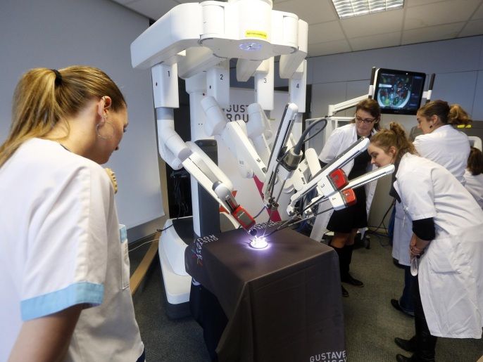 TO GO WITH AFP STORY BY ELIZABETH ZINGG Medical staff gather around the 'Da Vinci Xi' surgical robot as it carries out a demonstration during its presentation on November 26, 2014 at the Gustave Roussy Institute, Europe's leading cancer treatment centre, in Villejuif, south of Paris. With four articulated arms fitted with cameras and surgical instruments, a surgeon controls this latest generation of surgical robots from a console equipped with joysticks and pedals, and benefits of a three-dimensional image in high-definition. AFP PHOTO FRANCOIS GUILLOT