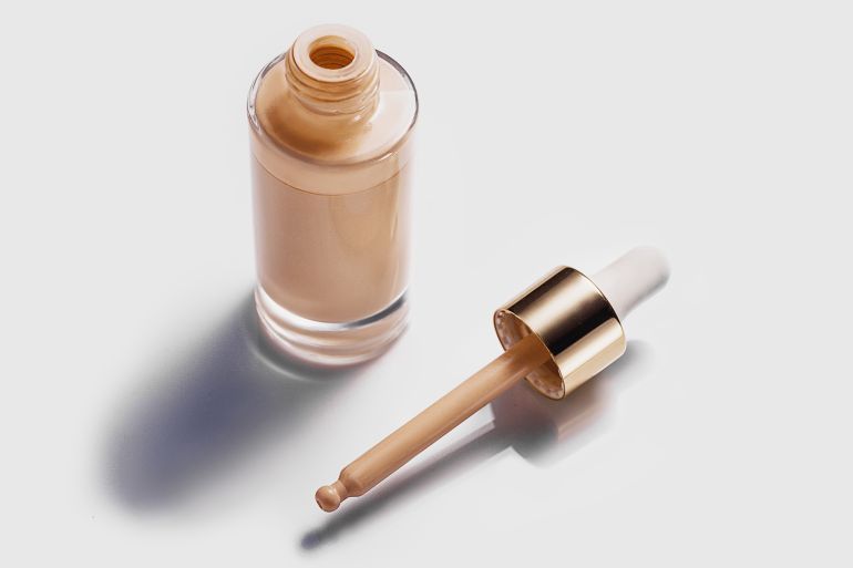 Thick Make-up Face Foundation in Bottle with Pipette on white background. Swatch smudge concealer, highlighter, smear face foundation on white background. Light beige or brown liquid powder. BB, CC cream makeup liquid foundation. Flat lay, copy space. Close-up.