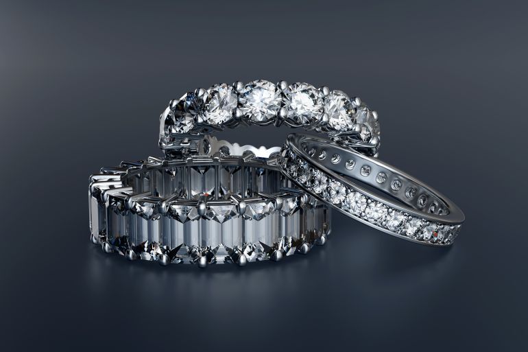 Three diamond eternity wedding bands on glossy blue background. 3D illustration