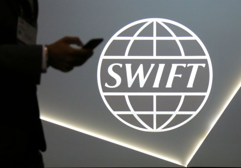A man using a mobile phone passes the logo of global secure financial messaging services cooperative SWIFT at the SIBOS banking and financial conference in Toronto, Ontario, Canada October 19, 2017. REUTERS/Chris Helgren