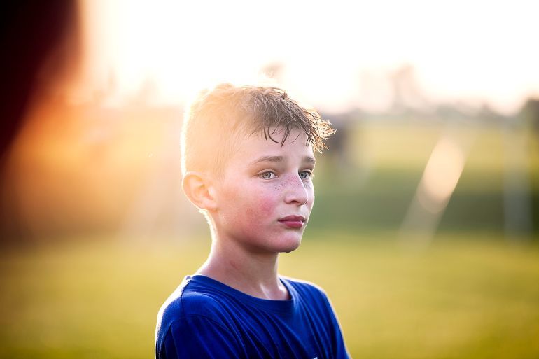 Sweaty 11 year old boy watching teammates playing soccer from sidelines - stock photo