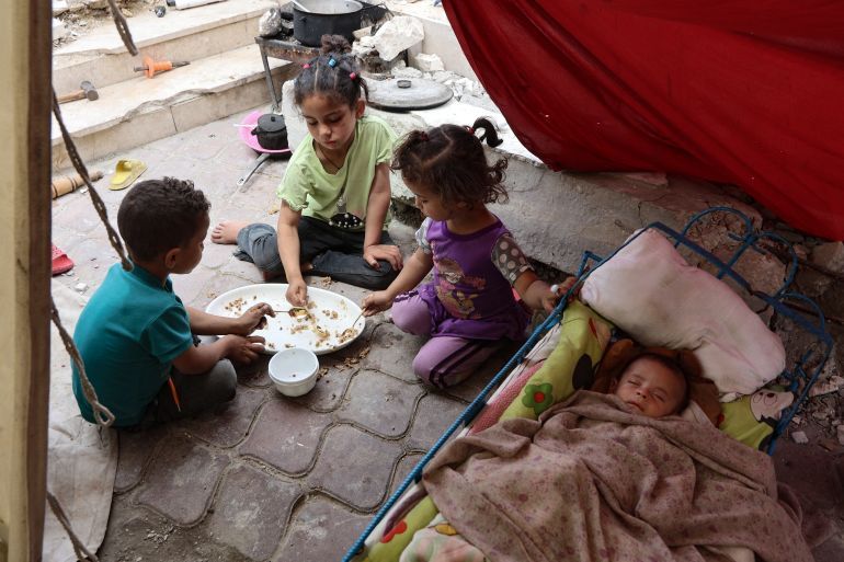 TOPSHOT - Palestinian children share a meal of rice as a baby sleeps, inside a tent at a displacement camp near Gaza City's port on May 22, 2025.