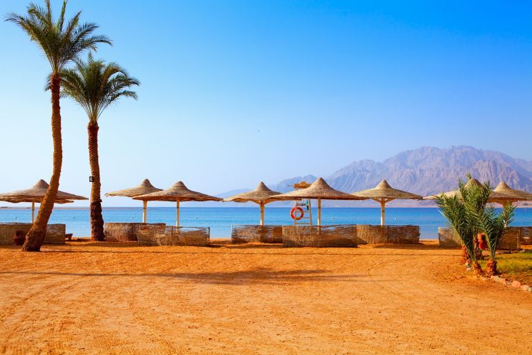 Egypt, sunny day on Dahab beach, beach umbrellas, sun loungers, rest, palm trees, seashore, red sea,