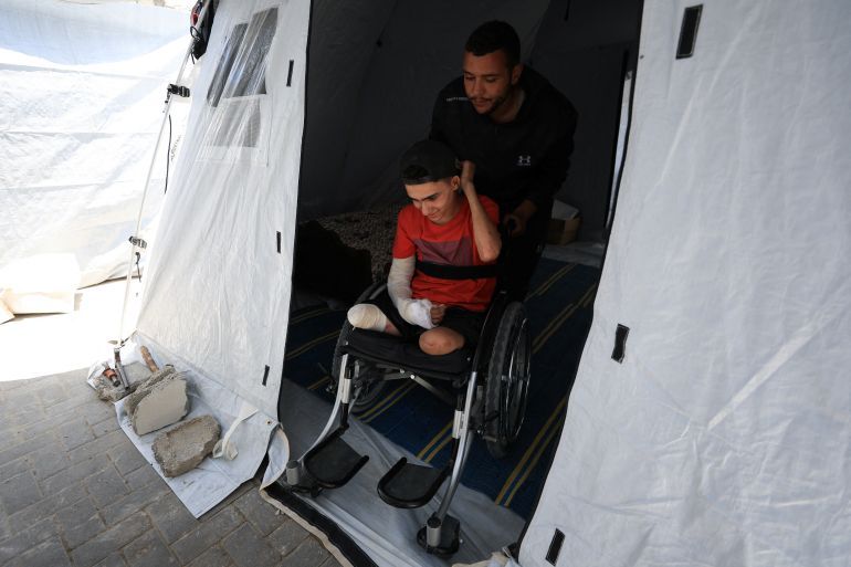 A Palestinian man pushes Ahmad Al-Ghalban, a 16-year-old Palestinian gymnast, who lost both his legs in an Israeli airstrike on Beit Lahiya, outside his tent as he sits in his wheelchair, in Gaza City, May 21, 2025. REUTERS/Dawoud Abu Alkas
