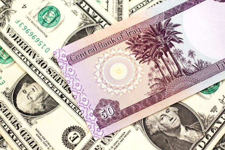 A purple Iraqi fifty dinar bank note close up in macro with an assortment of American one dollar bills