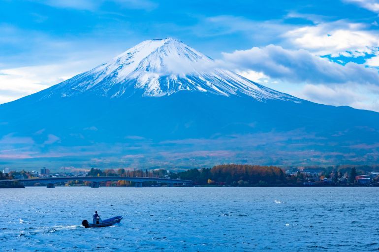 Japan. Mount Fuji with snow on top. Boat in the lake Kawaguchiko. Human on a boat on the ...
