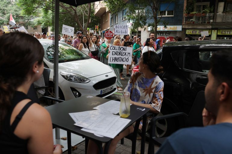 Tourists sitting at a terrace watch protesters during a demonstration against mass tourism in Barcelona, on June 15, 2025.
