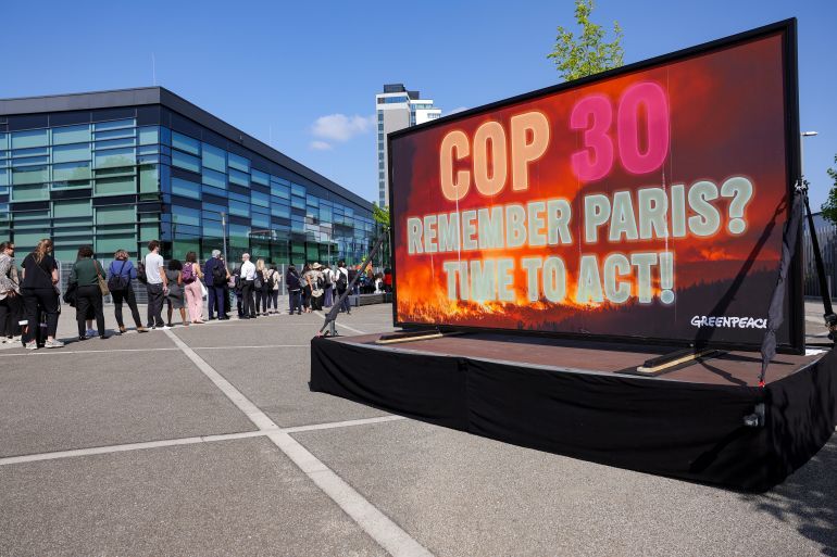 epa12178878 People stand in line as Greenpeace activists display a large screen in front of the Climate Change Conference in Bonn, Germany, 16 June 2025. The SB62 Climate Change Conference is the pre-sessional meeting for the COP30 Climate Change Conference to be held in Belem, Brazil in November 2025. EPA-EFE/CHRISTOPHER NEUNDORF