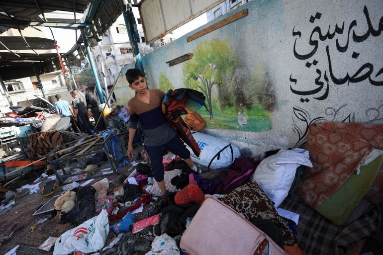 A Palestinian inspects the damage at a school sheltering displaced people, near a wall reading,