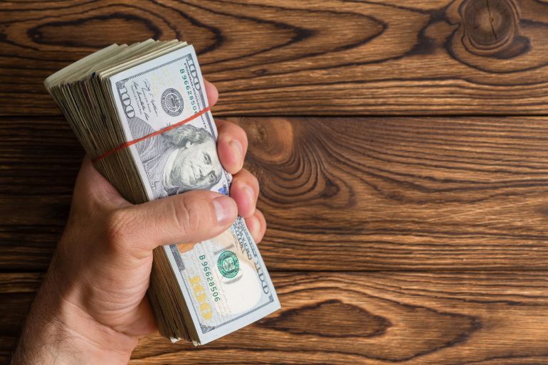 Man gripping a thick stack of 100 dollar bills or Benjamins in his hand over a rustic wood background with copy space