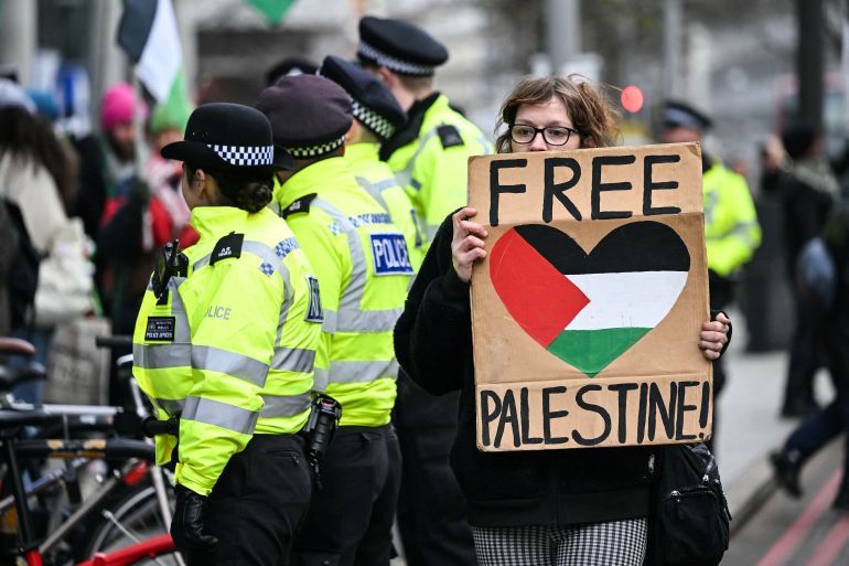 A pro-Palestinian supporter holds a placards as she walks past Met police officers while taking part in a 