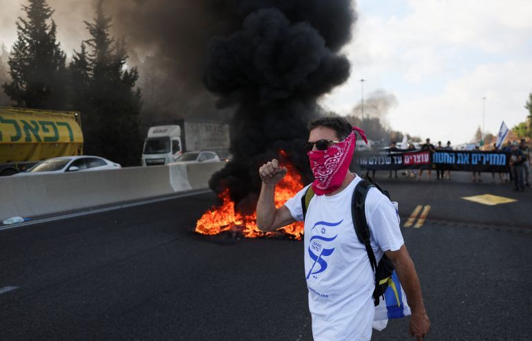 A man gestures in front of burning tyres as people block Israel's main highway connecting Jerusalem and Tel Aviv near Latrun after families of hostages have called for a nationwide strike to demand the return of all hostages and an end to the war in Gaza, Latrun Israel August 17,2025 REUTERS/Ronen Zvulun