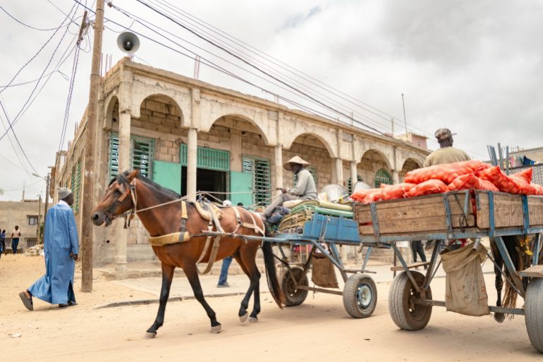 Merchants ride past the Great Mosque of Nietty Mbar in Thiaroye, a suburb of Dakar, Senegal, Friday, July 4, 2025.(AP Photo/Sylvain Cherkaoui)