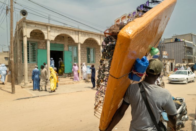 Merchantswalk past the Great Mosque of Nietty Mbar in Thiaroye, a suburb of Dakar, Senegal, Friday, July 4, 2025.(AP Photo/Sylvain Cherkaoui)